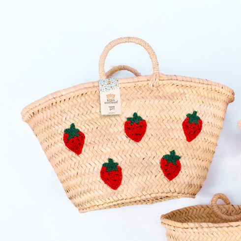 Hand-embroidered straw basket with multiple red strawberries, green leaves, and natural palm leaf texture