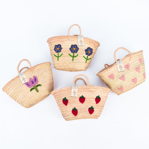 Hand-embroidered straw basket with multiple red strawberries, green leaves, and natural palm leaf texture