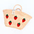 Hand-embroidered straw basket with multiple red strawberries, green leaves, and natural palm leaf texture