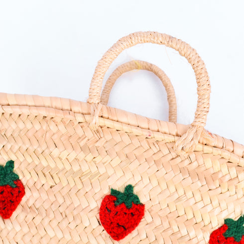 Hand-embroidered straw basket with multiple red strawberries, green leaves, and natural palm leaf texture