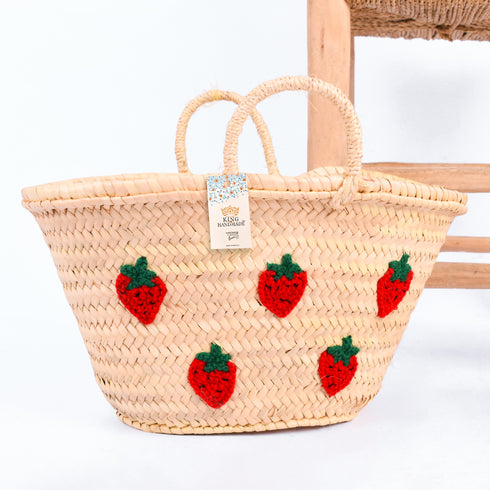 Hand-embroidered straw basket with multiple red strawberries, green leaves, and natural palm leaf texture