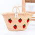 Hand-embroidered straw basket with multiple red strawberries, green leaves, and natural palm leaf texture