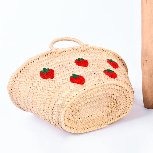 Hand-embroidered straw basket with multiple red strawberries, green leaves, and natural palm leaf texture