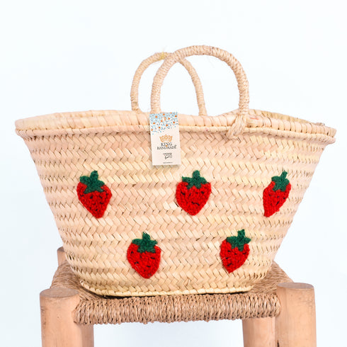 Hand-embroidered straw basket with multiple red strawberries, green leaves, and natural palm leaf texture