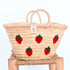 Hand-embroidered straw basket with multiple red strawberries, green leaves, and natural palm leaf texture