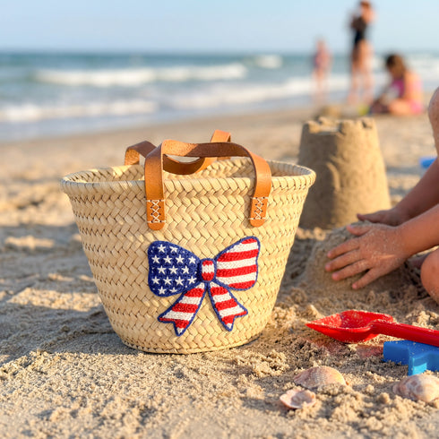 Personalized USA kids straw basket with embroidered American flag bow, small handwoven palm leaf tote with leather handles, custom name on back, patriotic children’s beach and birthday gift bag