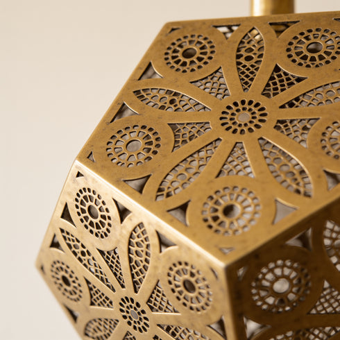 Close-up of a brass geometric metal lantern with intricate circular cutout patterns, showing its warm metallic finish against a soft neutral background.