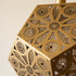 Close-up of a brass geometric metal lantern with intricate circular cutout patterns, showing its warm metallic finish against a soft neutral background.