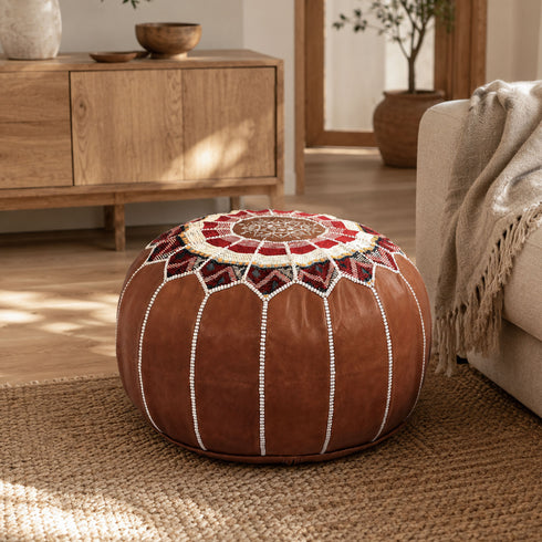 Dark tan round Moroccan leather pouf with Amazigh Berber motifs styled on a jute rug in a warm, modern living room