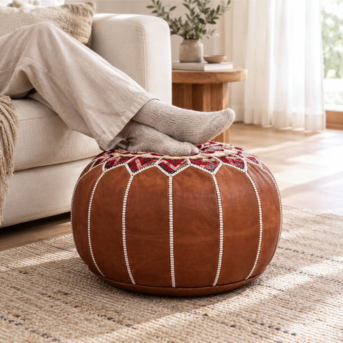 Person relaxing with feet in cozy socks resting on a dark tan round Moroccan pouf used as a footrest beside a sofa