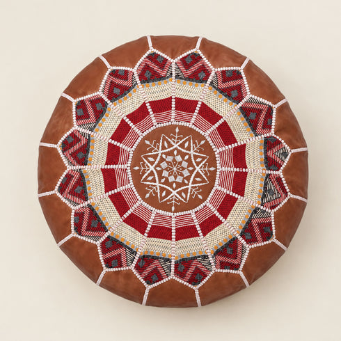 Top view of a stuffed dark tan round fusion pouf with intricate red, cream and white Amazigh Berber embroidered motif fabric
