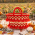 Handmade fire red tassel straw basket on a plaid blanket in a pumpkin patch with mini pumpkins, eucalyptus and wheat for Thanksgiving