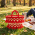 Fire red tassel straw basket with gold beads at an autumn park picnic with apples, a thermos and fallen leaves