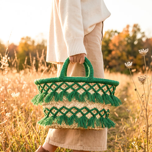 Model carrying a handmade Moroccan green tassel straw basket with gold beads through a golden autumn meadow