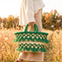 Model carrying a handmade Moroccan green tassel straw basket with gold beads through a golden autumn meadow