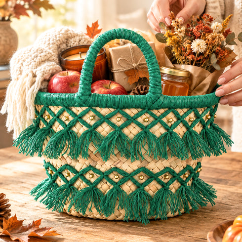 Handmade deep green tassel straw basket styled as a fall gift basket with apples, candle, honey jar and dried flowers on a wooden table