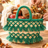 Handmade deep green tassel straw basket styled as a fall gift basket with apples, candle, honey jar and dried flowers on a wooden table