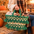 Handmade green tassel straw basket filled with Halloween treats and a plaid blanket on a hay bale at an autumn harvest hayride