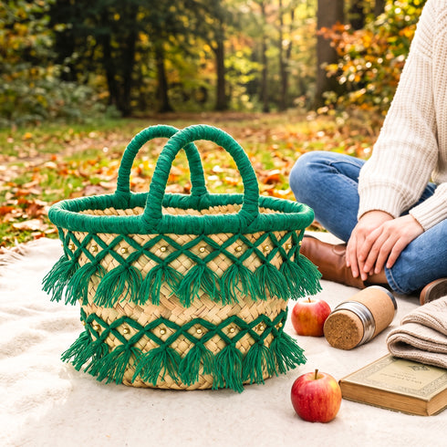 Green tassel straw basket with gold bead details on a woodland fall picnic blanket with apples, a cork thermos and an old book