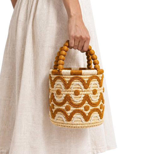 Artisan straw bucket bag with wooden bobbin bead handle carried with a flowing beige dress, handmade in Marrakech