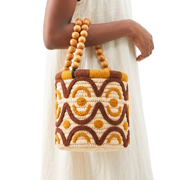 Handmade Moroccan raffia bucket bag with wooden bead handles worn on the forearm with a white linen dress