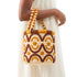 Handmade Moroccan raffia bucket bag with wooden bead handles worn on the forearm with a white linen dress