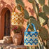 Handmade Moroccan raffia bucket bags in blue and ochre embroidery hanging against terracotta wall and cactus