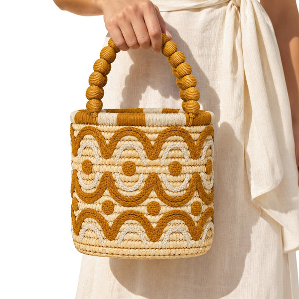 Close-up of handmade Moroccan raffia bucket bag with goldenrod and beige scalloped cotton embroidery and beaded top handle