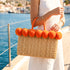 Orange pom pom wicker beach bag with matching handles carried on the forearm on a sunny yacht deck by the sea
