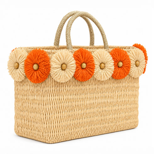 Handmade Moroccan wicker tote bag with braided straw handles and orange and natural raffia flowers on white background