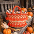 Handmade orange tassel straw basket filled with Halloween candy on a rustic porch bench with pumpkins and Indian corn