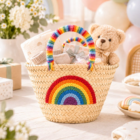 Rainbow baby gift basket with embroidered rainbow icon holding a teddy bear, muslin blanket, booties and gift box