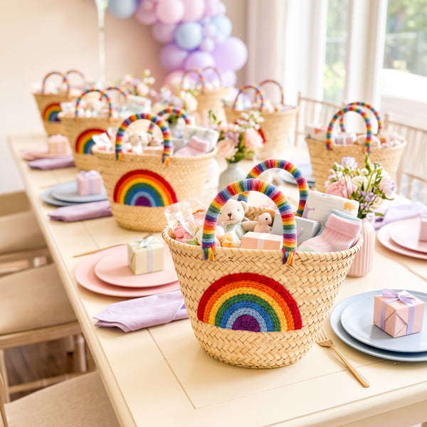Rainbow baby shower favor baskets filled with guest gifts on a pastel party table with balloons and flowers