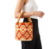 Woman carrying small raffia bucket bag with wooden bead handle on her forearm with black trousers