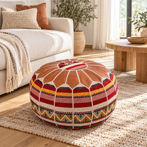 Tan round Moroccan pouf with leather top and Amazigh Berber motif fabric styled on a woven rug beside a cream sofa in a bright living room