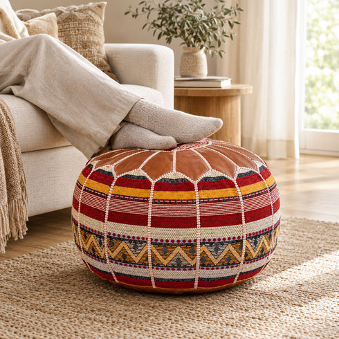 Person relaxing with feet in cozy socks resting on a tan round Moroccan pouf with Amazigh Berber motif fabric, used as a footrest beside a sofa