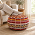 Person relaxing with feet in cozy socks resting on a tan round Moroccan pouf with Amazigh Berber motif fabric, used as a footrest beside a sofa