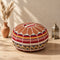 Tan round fusion Moroccan pouf with leather top and red, gold and cream Amazigh Berber motif fabric sides beside pampas grass and a Moroccan lantern