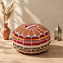 Tan round fusion Moroccan pouf with leather top and red, gold and cream Amazigh Berber motif fabric sides beside pampas grass and a Moroccan lantern