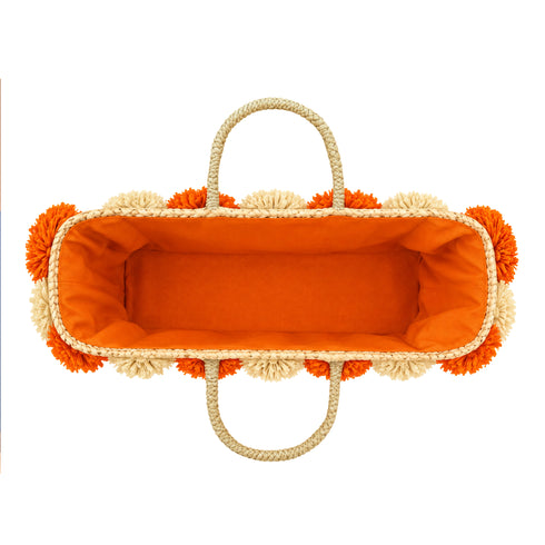 Top view of a handwoven wicker tote bag with orange fabric lining, braided straw handles and raffia flowers around the rim