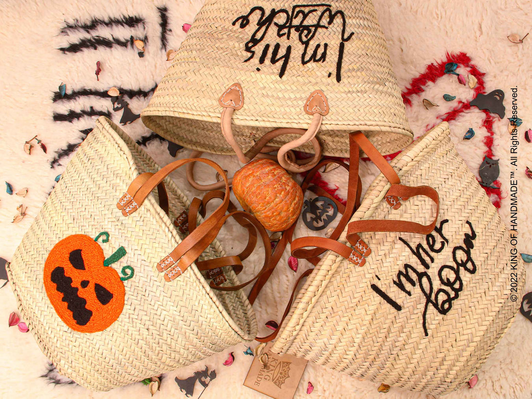 A black trick-or-treat bucket with an orange jack-o-lantern face and a sturdy plastic handle.