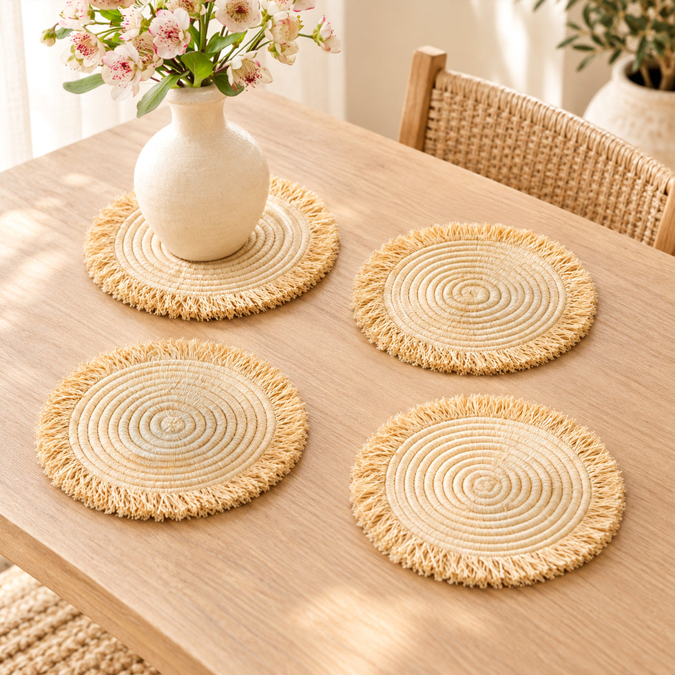 Four handwoven Moroccan fringe table mats on an oak table, one styled as a centerpiece mat under a flower vase