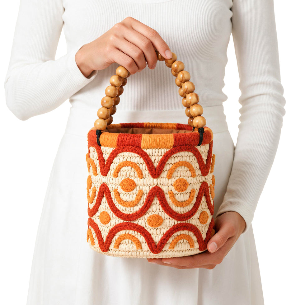 Boho raffia bucket bag with orange embroidery and wooden bead handle styled with a white eyelet dress