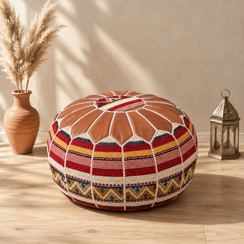 Tan round fusion Moroccan pouf with leather top and red, gold and cream Amazigh Berber motif fabric sides beside pampas grass and a Moroccan lantern